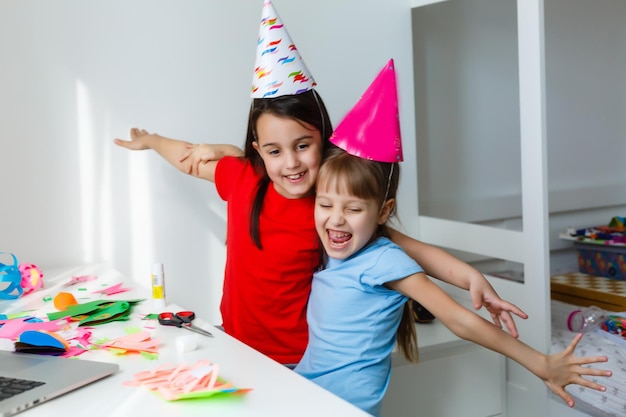 Festa di compleanno online per bambini. Bambine in abiti, cappello celebrano le vacanze con gli amici. Conferenza, videochiamata su laptop, computer. Quarantena, pandemia di coronavirus covid-19.