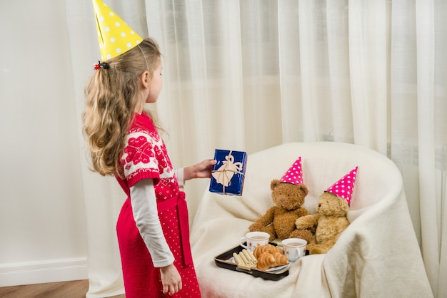 Festa di compleanno, ragazzo in cappello festivo che gioca con gli orsacchiotti.