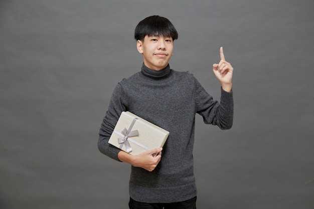Festa di Natale e concetto di vacanze. Giovane uomo asiatico con confezione regalo studio shot, isolato su sfondo grigio