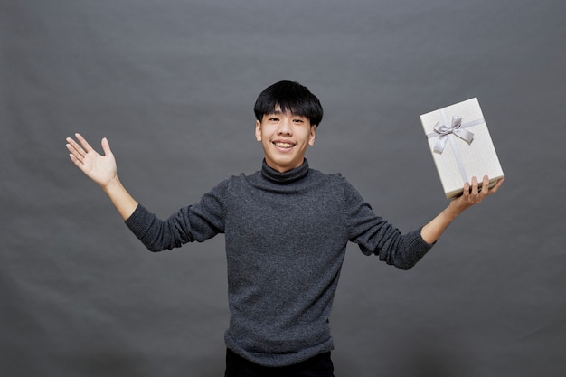 Festa di Natale e concetto di vacanze. Giovane uomo asiatico con confezione regalo studio shot, isolato su sfondo grigio