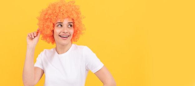 Festa divertente parrucca allegra ragazza divertente con look di fantasia che indossa una parrucca di capelli arancioni su sfondo giallo cool