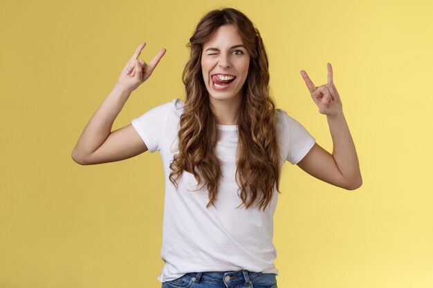 Festa fantastica divertendosi. Audace ragazza spensierata attraente godere di un eccellente evento spettacolo rock-n-roll heavy metal gesto che mima espressioni divertenti strizza l'occhio bastone lingua stare in piedi sfondo giallo divertito.