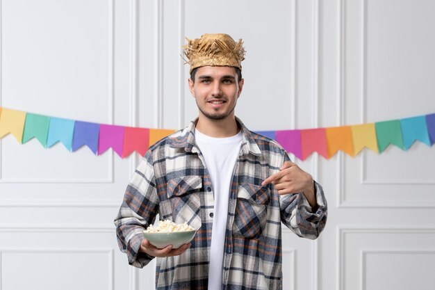 Festa junina bel ragazzo adorabile con cappello di paglia e camicia che celebra il festival con una ciotola di popcorn