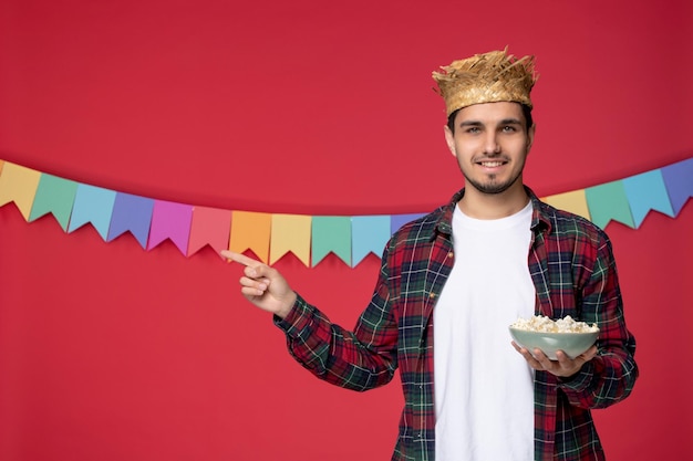 Festa junina felice ragazzo carino che indossa un cappello di paglia che celebra il festival brasiliano con una ciotola di popcorn