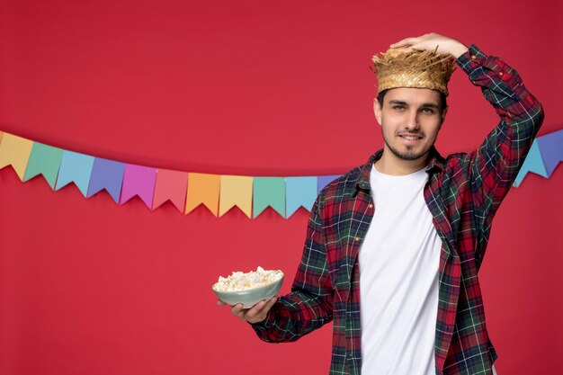 Festa junina felice ragazzo carino che indossa un cappello di paglia che celebra il festival brasiliano mangiando gustosi popcorn