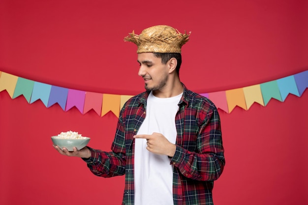 Festa junina felice ragazzo carino che indossa un cappello di paglia che celebra il festival brasiliano vuole mangiare il mais