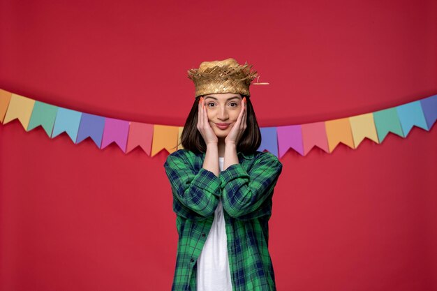 Festa junina giovane ragazza carina in camicia verde che celebra il festival brasiliano tenendo il viso