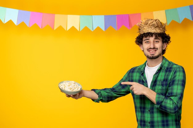 Festa junina giovane ragazzo carino con cappello di paglia e bandiere colorate festival brasiliano che punta al popcorn