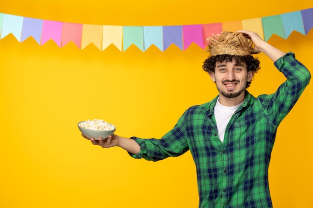 Festa junina giovane ragazzo carino con cappello di paglia e bandiere colorate festival brasiliano che tiene popcorn