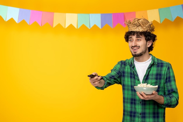 Festa junina giovane ragazzo carino con cappello di paglia e bandiere colorate festival brasiliano guardando la tv popcorn