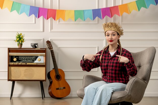 Festa junina ragazza carina con cappello di paglia brasiliano di mezza estate con chitarra radiofonica retrò che punta a se stessa