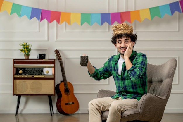 Festa junina ragazzo carino con cappello di paglia con radio retrò e bandiere colorate che tengono una tazza di caffè