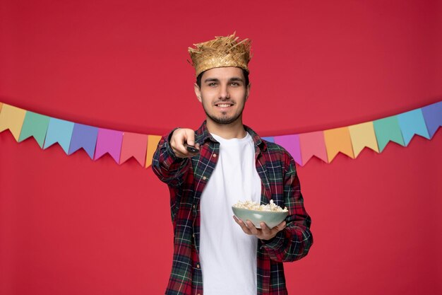 Festa junina sorridente ragazzo carino che indossa un cappello di paglia che celebra il festival brasiliano guardando il programma televisivo