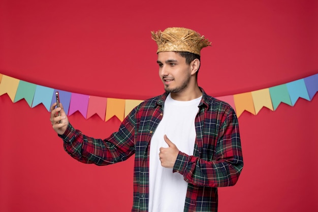 Festa junina sorridente ragazzo carino che indossa un cappello di paglia che celebra il festival brasiliano prendendo selfie