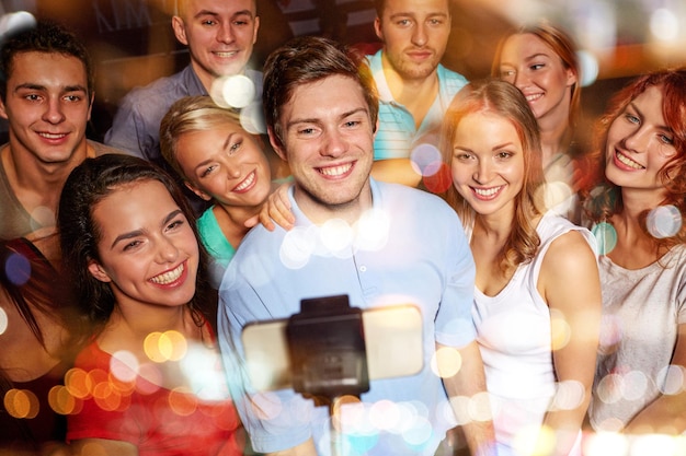 festa, tecnologia, vita notturna e concetto di persone - amici sorridenti con smartphone e monopiede che prendono selfie nel club