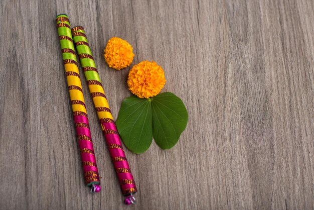 Feste indiane Dussehra e Navratri che mostrano foglie d'oro Bauhinia racemosa e fiori di marigold con bastoncini di Dandiya su uno sfondo di legno