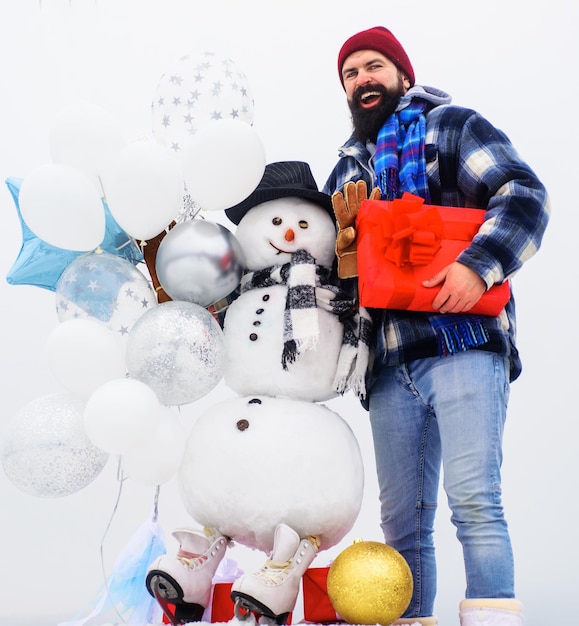 Feste invernali felici uomo barbuto in abiti invernali con scatola regalo e uomo di neve in sciarpa cappello e