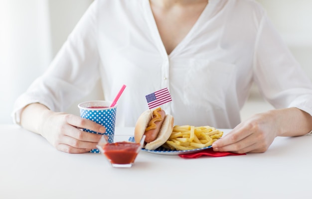 feste nazionali, celebrazione, cibo e concetto di patriottismo - primo piano di donna che mangia hot dog e patatine fritte con bevanda in tazza di carta usa e getta il 4 luglio alla festa del giorno dell'indipendenza americana