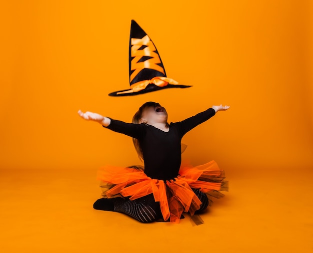 Festeggiando Halloween. Una bambina vestita da strega tiene in mano un secchio di zucche su sfondo giallo.