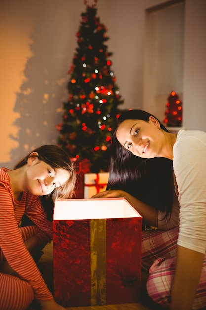 Festiva madre e figlia aprendo un regalo di Natale incandescente