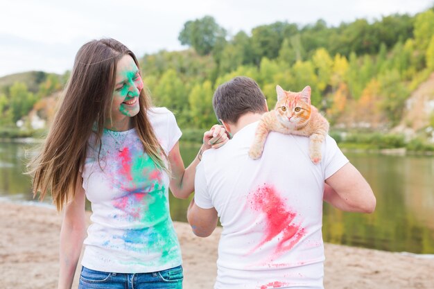 Festival holi, turismo e concetto di natura - Ritratto di donna e uomo con gatto ricoperto di polvere multicolore.