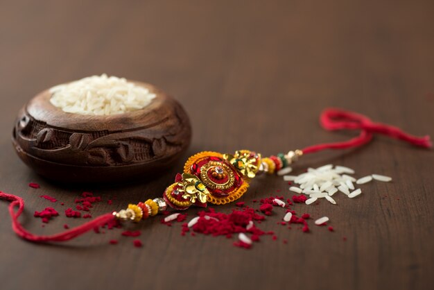 Festival indiano: Raksha Bandhan sullo sfondo con un elegante Rakhi, chicchi di riso e Kumkum. Un cinturino da polso tradizionale indiano che è un simbolo dell'amore tra fratelli e sorelle.