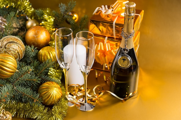 Festive Still Life - Antico orologio da tasca drappeggiato su bottiglia di champagne con paio di occhiali su sfondo dorato con regali di Natale e sempreverde decorato con palline di Natale e orpelli dorati