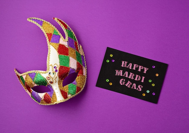 Festosa e colorata mardi gras o maschera di carnevale e biglietto di auguri sulla parete viola.Piano laico, vista dall'alto, spazio di copia