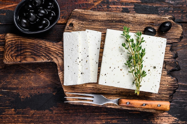 Feta di formaggio fresco con timo e olive. Fondo in legno scuro. Vista dall'alto.