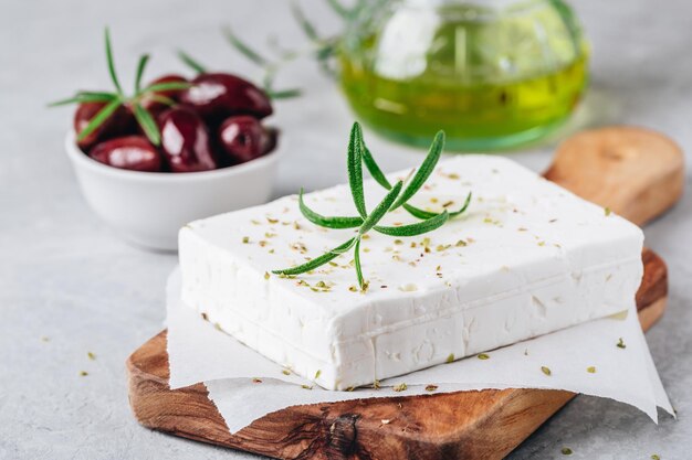 Feta di formaggio greco fatto in casa con rosmarino ed erbe aromatiche su tagliere di legno con olio d'oliva e olive