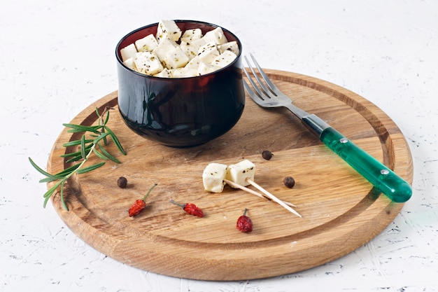 Feta marinato in un piatto su una tavola di legno con spezie su uno sfondo bianco