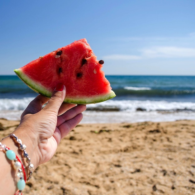 Fetta di anguria matura nella mano delle ragazze Sfondo spiaggia mare e cielo blu