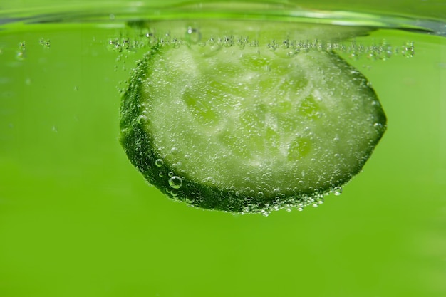 Fetta di cetriolo in acqua su sfondo verde