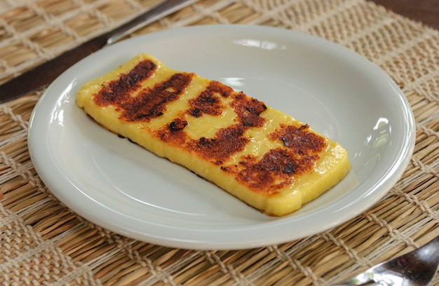 Fetta di formaggio caglio al forno su un piatto bianco su un tavolo di legno.