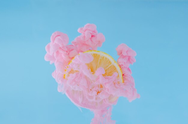 Fetta di limone con messa a fuoco parziale della dissoluzione del colore rosa del poster in acqua per il concetto estivo