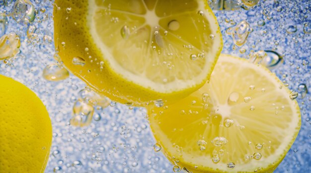 Fetta di limone sott'acqua in acqua gassata o limonata con bollicine Cocktail frizzante tonico e tonico rinfrescante Primo piano di limoni e cubetti di ghiaccio in vetro Lime in spruzzi di acqua frizzante bevanda fredda