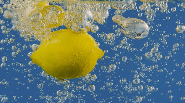 Fetta di limone sott'acqua in acqua gassata o limonata con bollicine Cocktail frizzante tonico e tonico rinfrescante Primo piano di limoni e cubetti di ghiaccio in vetro Lime in spruzzi di acqua frizzante bevanda fredda