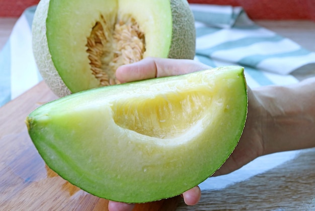 Fetta di melone maturo fresco succoso in mano con frutta intera sfocata sullo sfondo