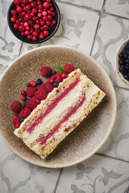 Fetta di pan di spagna con ripieno di lamponi e crema al cocco guarnita con frutti di bosco freschi