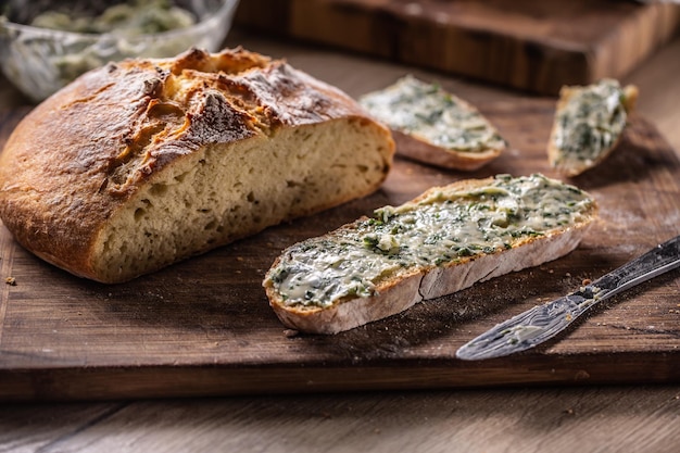 Fetta di pane con burro alle erbe accanto a una pagnotta croccante appena sfornata accanto ad essa