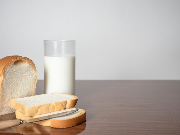 Fetta di pane della pagnotta con il coltello con un bicchiere di latte sullo spazio della copia del tavolo