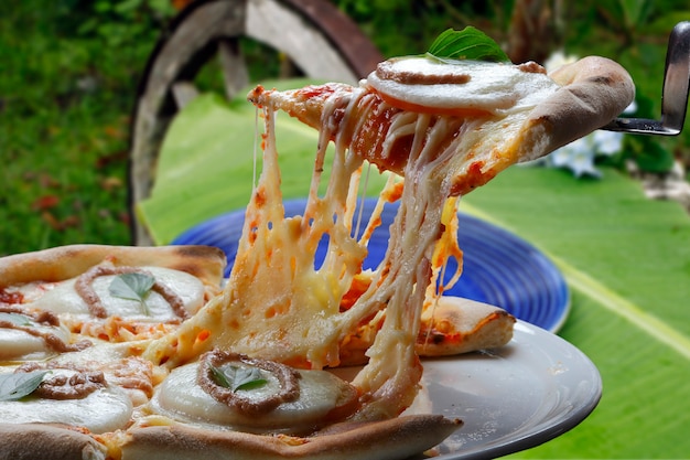 Fetta di pizza calda con formaggio fondente con forno a legna sullo sfondo.