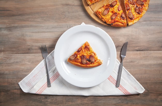 Fetta di pizza su piatto, forchetta, coltello su tavola di legno. Pizza in tavola rotonda
