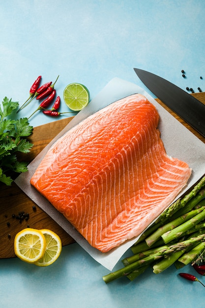 Fetta di salmone fresco su un tagliere di legno con erbe aromatiche fresche e asparagi sul tavolo. ricetta di cucina. sfondo di cibo. prodotti ittici freschi