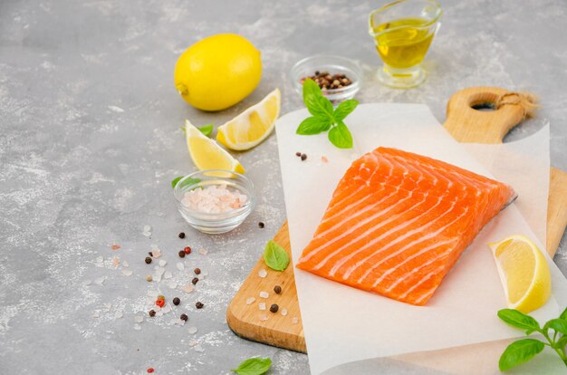 Fetta di salmone pesce rosso con limone, olio d'oliva, basilico fresco e spezie su una tavola di legno su un muro grigio. Copia spazio.