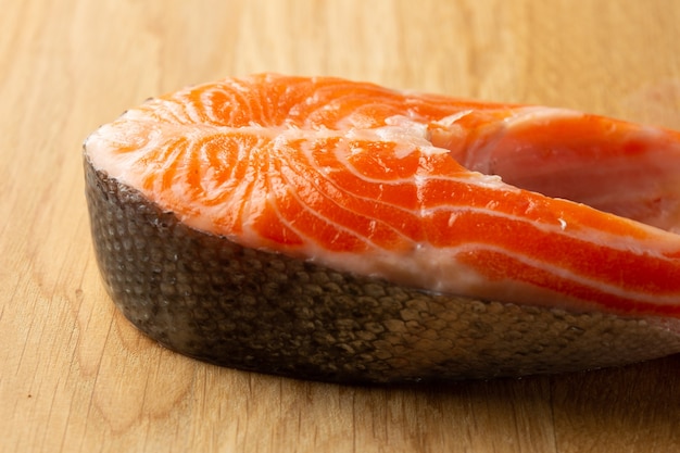 Fetta di salmone rosso crudo sdraiata sul tavolo di legno e dall'aspetto fresco