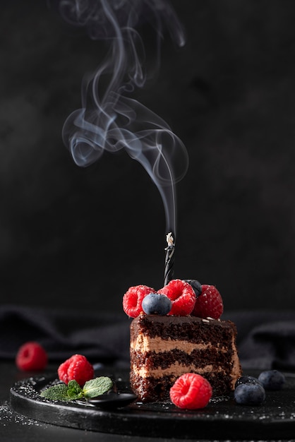 Fetta di torta al cioccolato artigianale con frutti di bosco freschi e candela di compleanno, primo piano