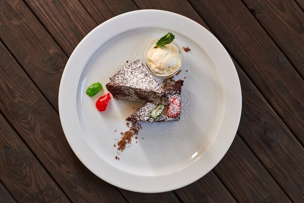 Fetta di torta al cioccolato con frutta candita, menta e gelato su un piatto