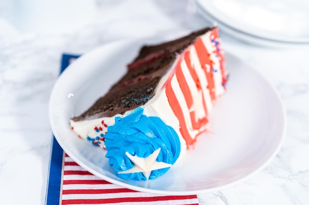 Fetta di torta al cioccolato del 4 luglio decorata con glassa di crema al burro bianca e blu rossa su un piatto bianco