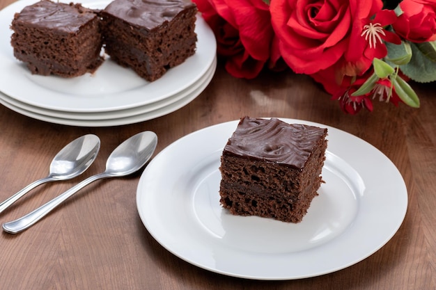 Fetta di torta al cioccolato ricoperta di cioccolato servita ghiacciata ad un bouquet di rose rosse